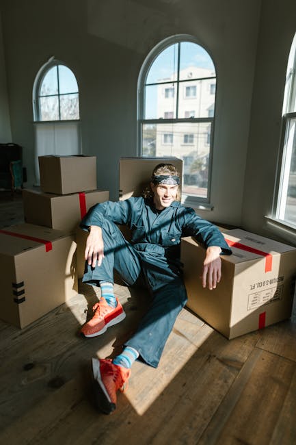 A professional removal technician from Removal Companies Stockwell is inside a bright, spacious room with light-colored wooden flooring and two large arched windows allowing natural light to fill the 